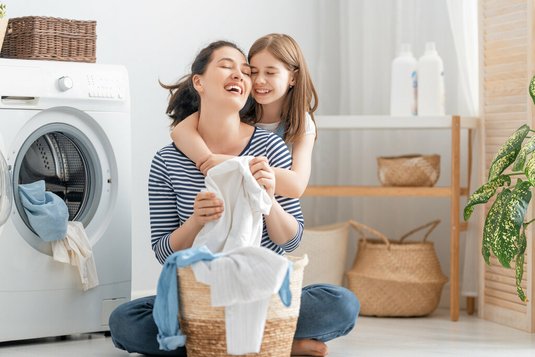 Haus-Mutter-Tochter-Wohnen-Serie-18-45 Junge Mutter und kleine Helferin haben Spaß beim Waschen zu Hause.