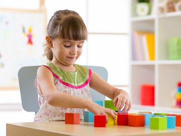 Mädchen beginnt Bausteine auf Tisch zu stapeln und steht für Planung und Finanzierungssicherheit durch den Hausbau Schutzbrief